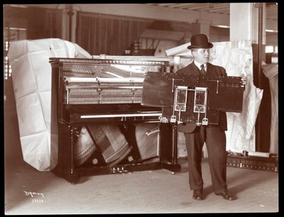 A Piano by Ricca und Son Piano Co. with a Man Adjacent Holding Up Part of the Piano Works by Byron Company